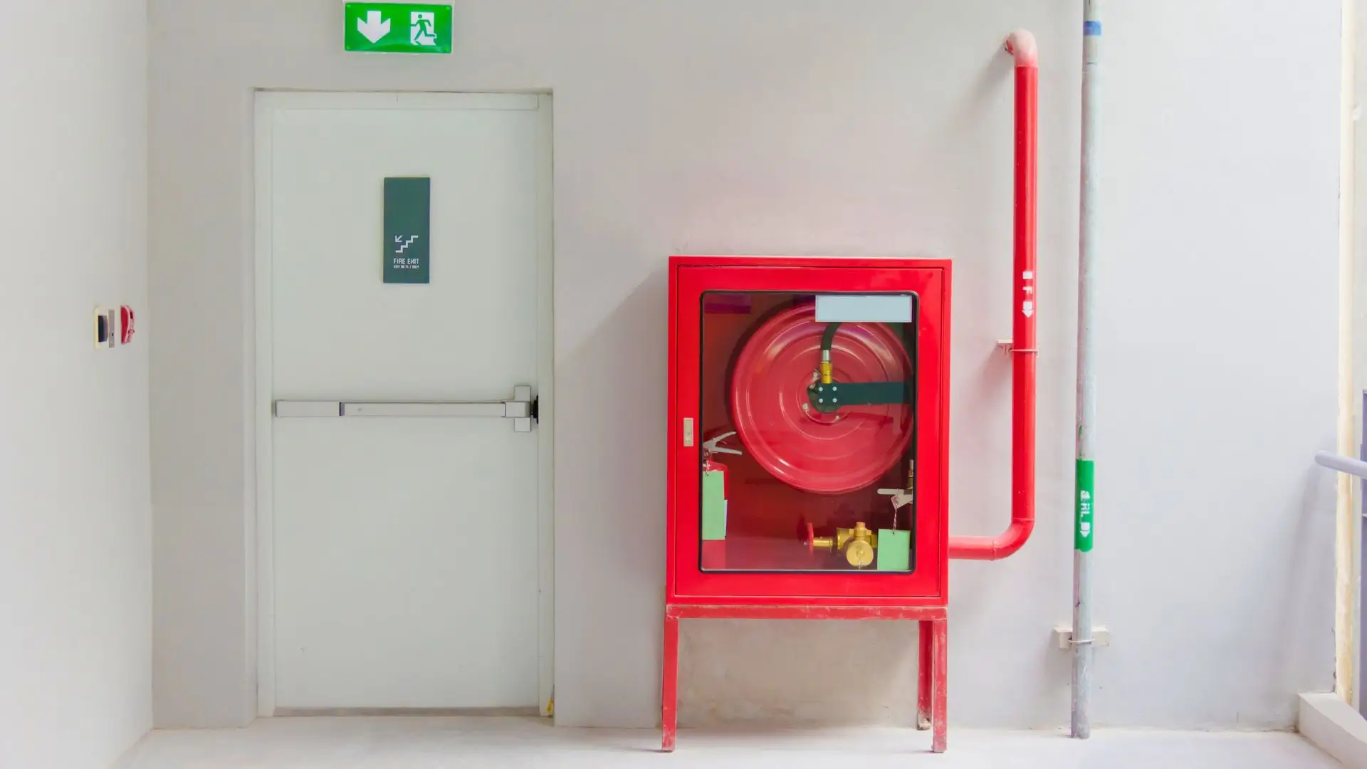 Red fire hose cabinet with hose reel beside a white exit door and a green emergency exit sign above it.