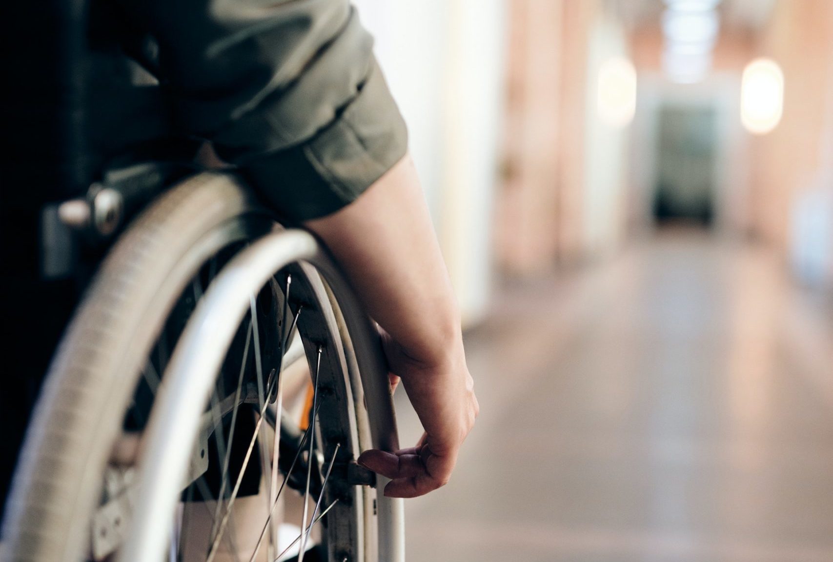 Close-up of a person in a wheelchair navigating a brightly lit hallway with soft focus in the background.