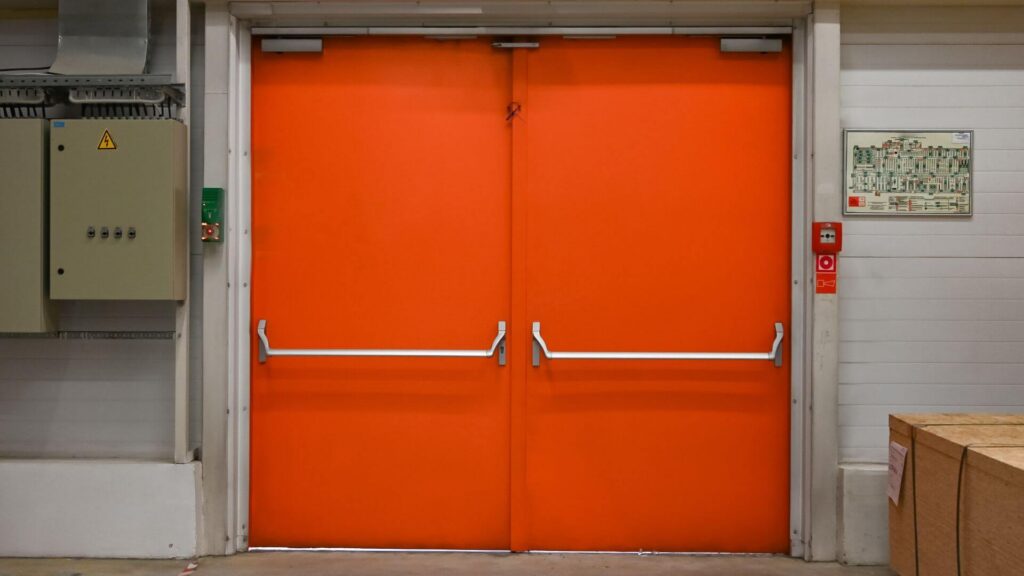 What are fire rated commercial doors? Double orange fire rated egress doors with panic hardware in industrial facility.
