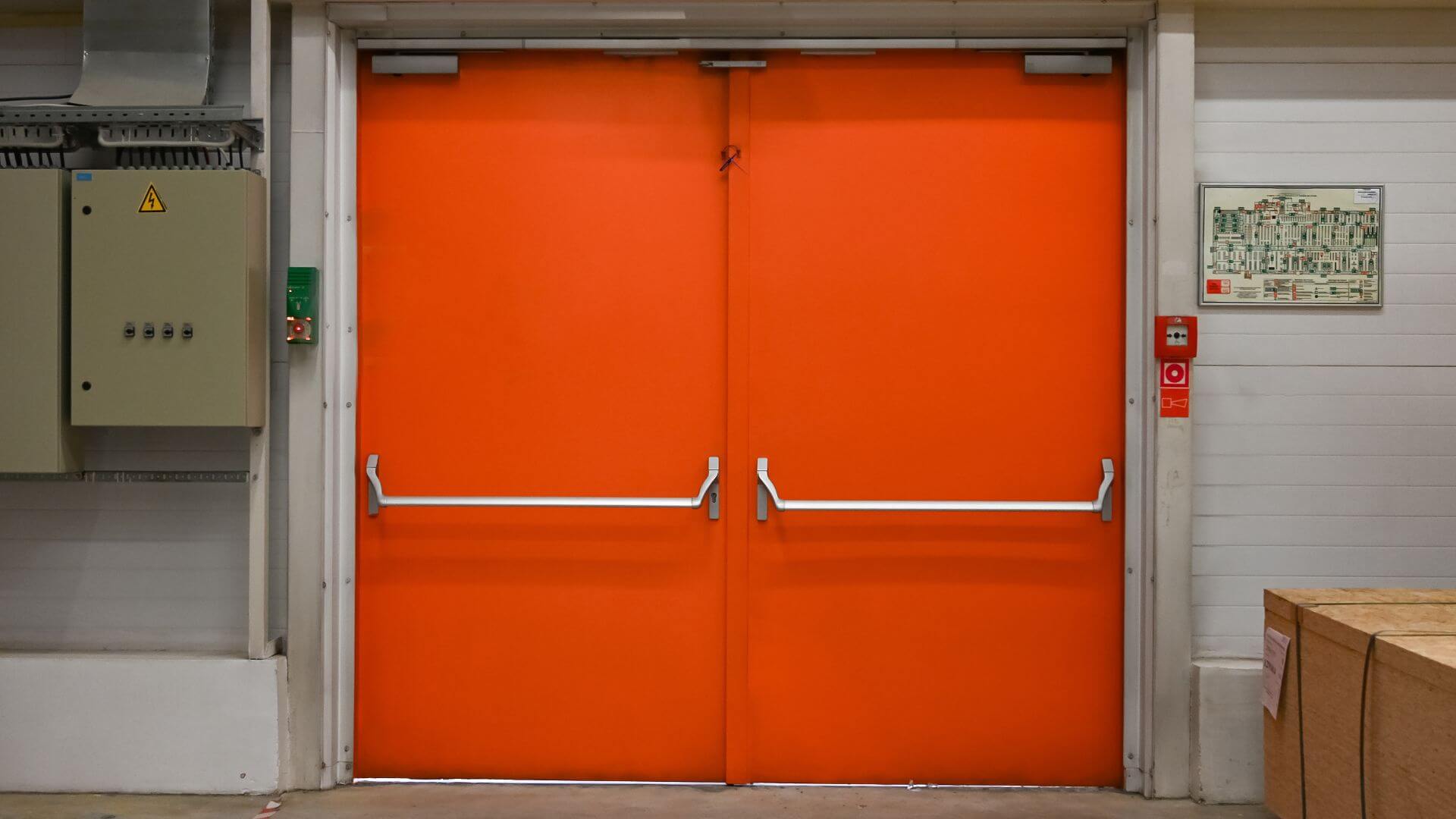 What are fire rated commercial doors? Double orange fire rated egress doors with panic hardware in industrial facility.